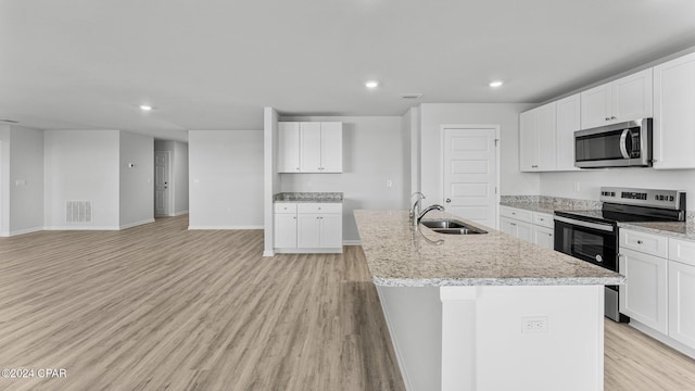 kitchen featuring stainless steel appliances, a sink, visible vents, light wood-type flooring, and a center island with sink