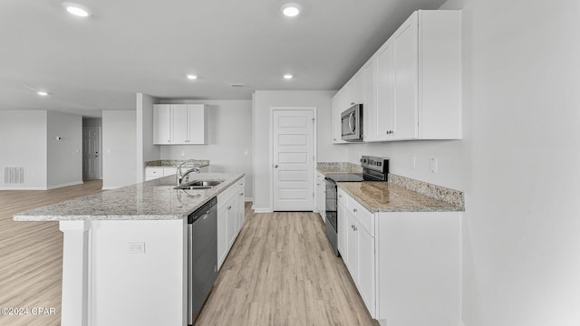 kitchen featuring appliances with stainless steel finishes, a sink, light stone counters, and light wood finished floors