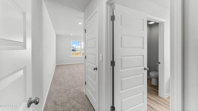 hallway featuring light colored carpet and baseboards