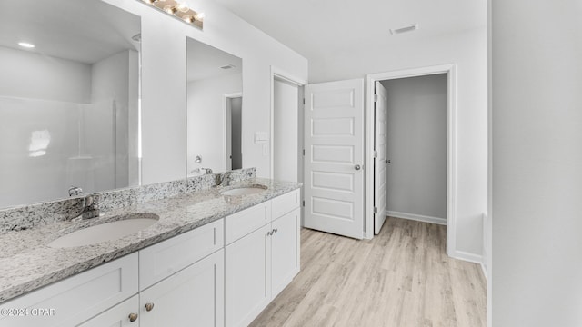 full bath with double vanity, visible vents, a sink, and wood finished floors