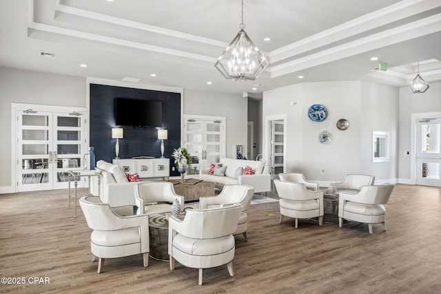 living area featuring a tray ceiling, a chandelier, wood finished floors, and french doors