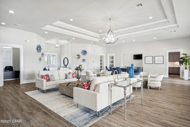 living area with a tray ceiling, visible vents, and wood finished floors