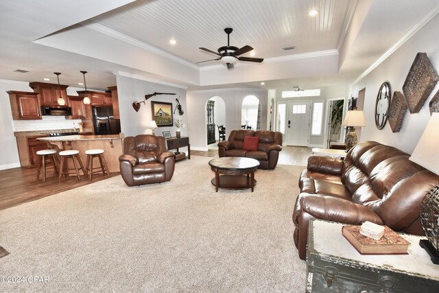 living room featuring wood-type flooring, a raised ceiling, crown molding, and ceiling fan