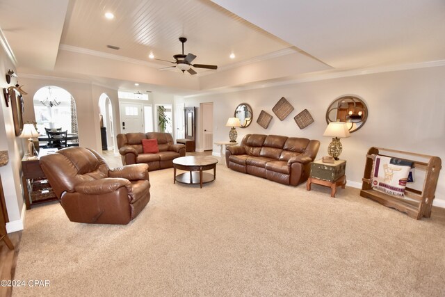 carpeted living room with ceiling fan with notable chandelier, a tray ceiling, and crown molding