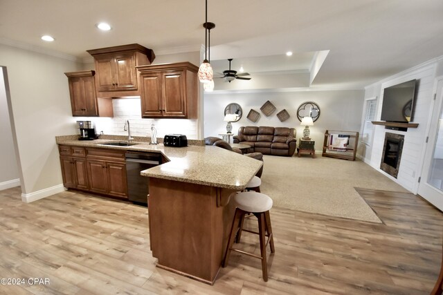 kitchen with light hardwood / wood-style floors, sink, kitchen peninsula, stainless steel dishwasher, and a kitchen bar