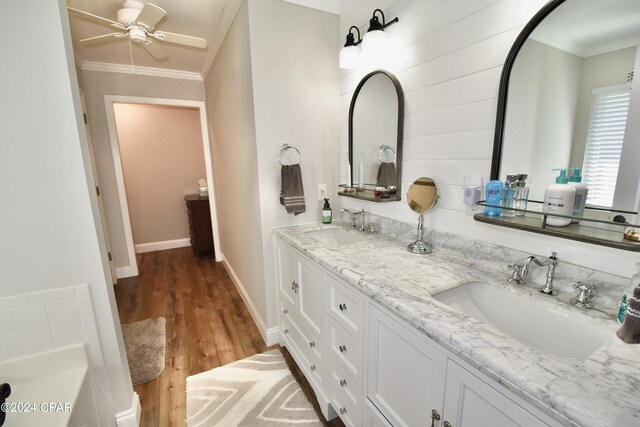 bathroom with wood-type flooring, a tub to relax in, ornamental molding, ceiling fan, and vanity