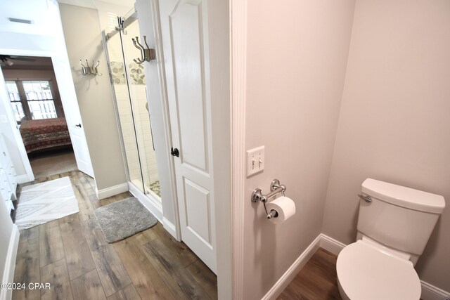 bathroom with wood-type flooring, toilet, and a shower with door