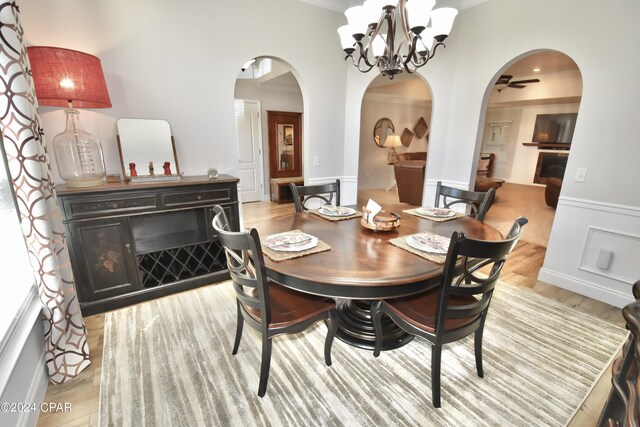 dining room with ceiling fan with notable chandelier, a fireplace, ornamental molding, and light hardwood / wood-style flooring