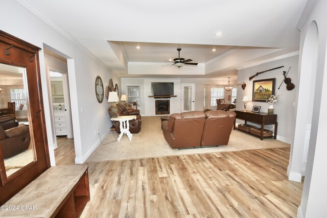 living room featuring ceiling fan, a tray ceiling, ornamental molding, and light hardwood / wood-style flooring