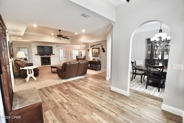 living room featuring ceiling fan with notable chandelier, light wood-type flooring, a tray ceiling, and crown molding