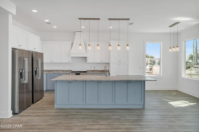 kitchen with light wood finished floors, white cabinetry, custom exhaust hood, and stainless steel appliances