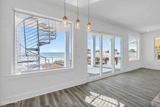 unfurnished dining area featuring a wealth of natural light, a water view, baseboards, and wood finished floors