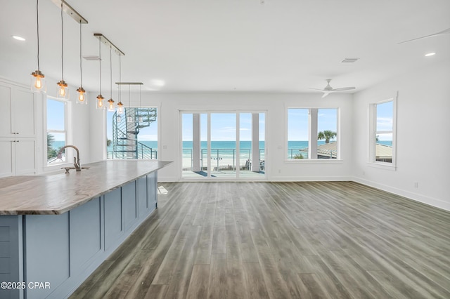 unfurnished living room featuring a healthy amount of sunlight, a water view, baseboards, and wood finished floors