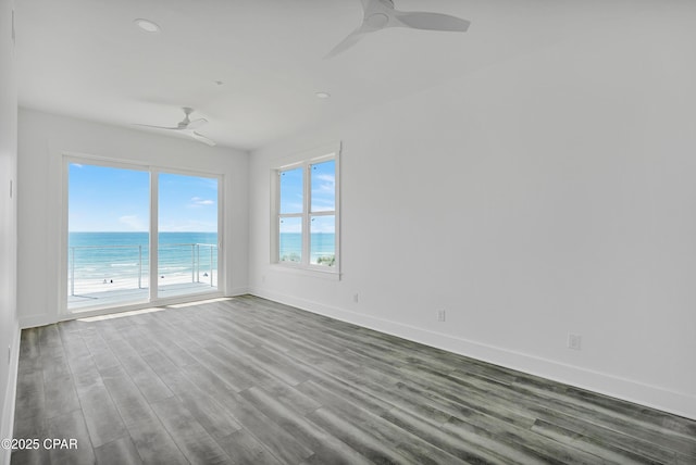 spare room with baseboards, a water view, ceiling fan, and wood finished floors