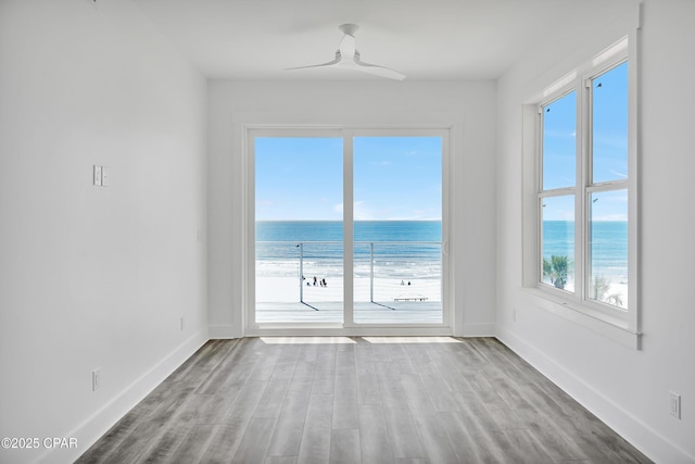 unfurnished room featuring a water view, baseboards, and wood finished floors