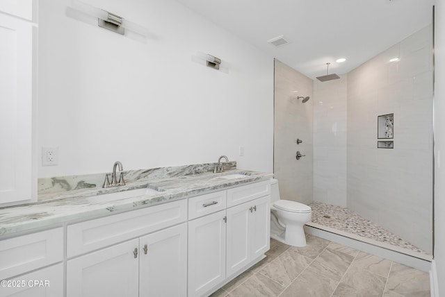 bathroom with visible vents, a sink, a tile shower, and toilet