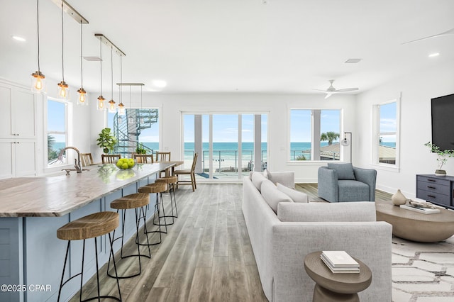 living room featuring a ceiling fan, visible vents, light wood finished floors, and baseboards