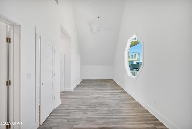 corridor featuring vaulted ceiling, baseboards, and wood finished floors