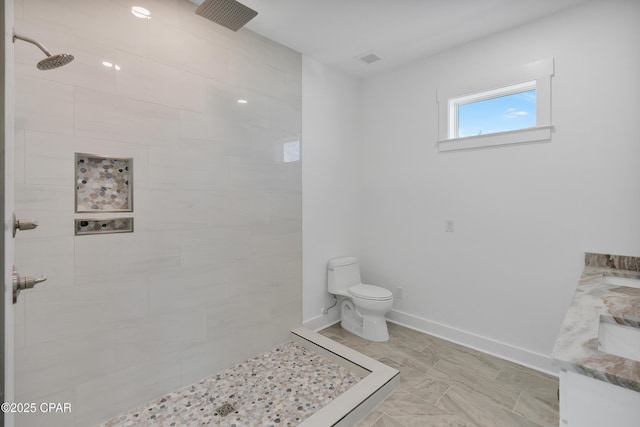 bathroom featuring a tile shower, toilet, vanity, and baseboards