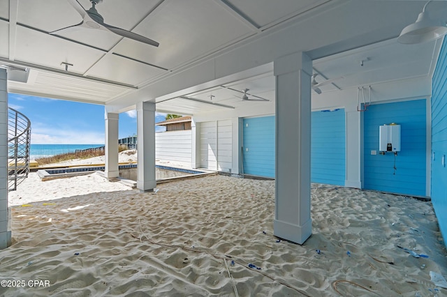 view of patio / terrace with water heater, a water view, a view of the beach, and a ceiling fan