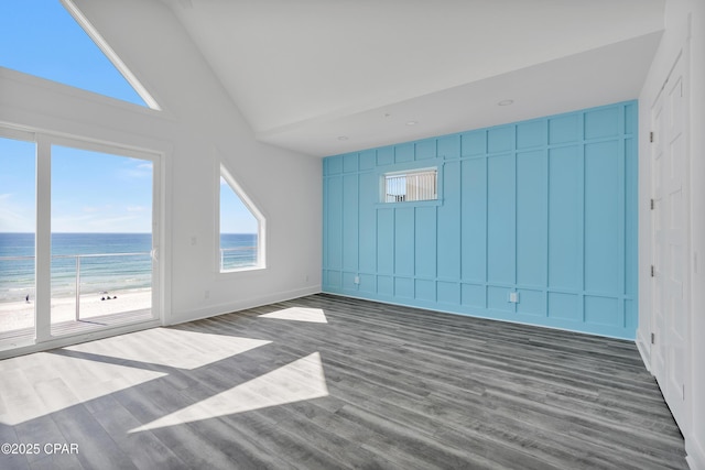 unfurnished room with a water view, dark wood-type flooring, a beach view, baseboards, and vaulted ceiling