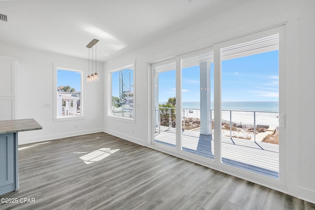 unfurnished dining area featuring visible vents, a water view, baseboards, and wood finished floors