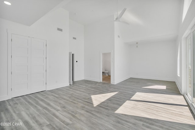 empty room with visible vents, high vaulted ceiling, baseboards, and wood finished floors