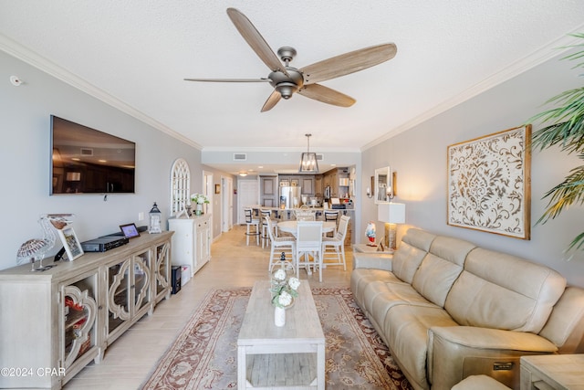 living room with light wood finished floors, visible vents, ornamental molding, a ceiling fan, and a textured ceiling