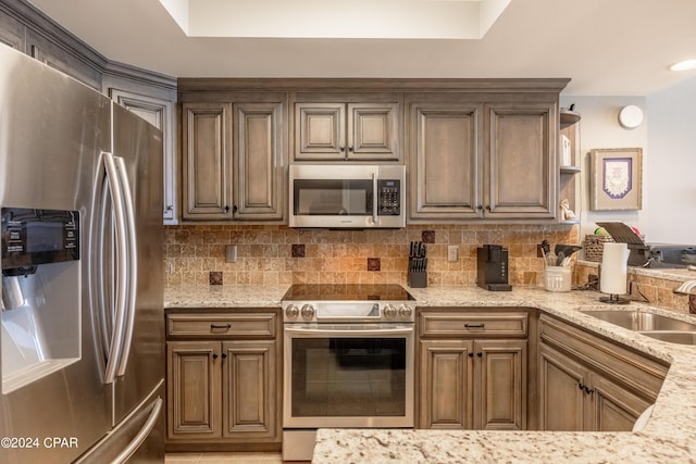 kitchen featuring stainless steel appliances, a sink, light stone counters, and tasteful backsplash