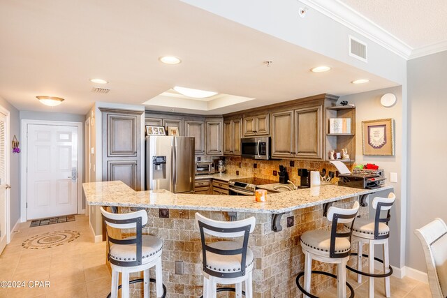 kitchen with appliances with stainless steel finishes, a kitchen breakfast bar, kitchen peninsula, light stone countertops, and ornamental molding