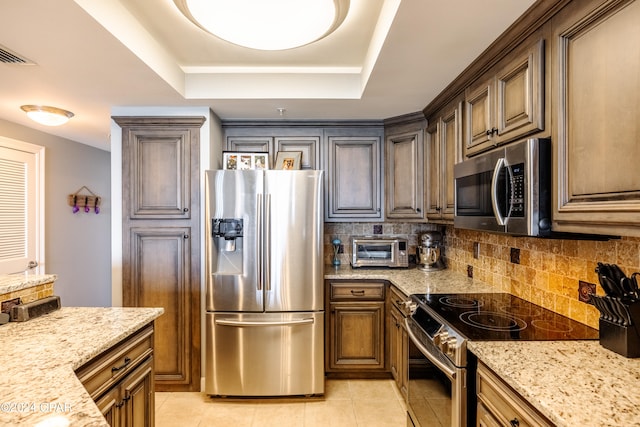 kitchen with stainless steel appliances, light stone counters, a raised ceiling, and light tile patterned flooring