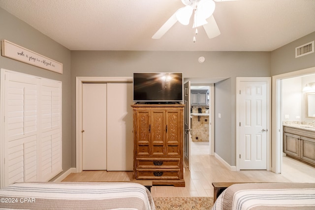 bedroom with ceiling fan, light hardwood / wood-style floors, a textured ceiling, a closet, and ensuite bathroom