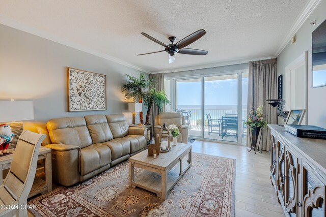 living room with a textured ceiling, a water view, ornamental molding, and ceiling fan