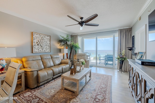 living room featuring a textured ceiling, light wood-style flooring, a water view, a ceiling fan, and crown molding