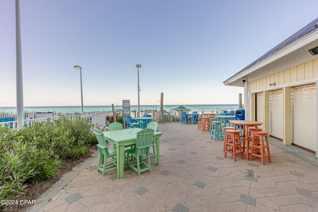 view of patio / terrace featuring outdoor dining space, a water view, a beach view, and a bar