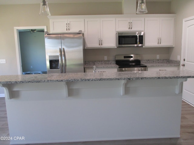 kitchen with appliances with stainless steel finishes, white cabinetry, light stone countertops, a kitchen island with sink, and dark hardwood / wood-style floors