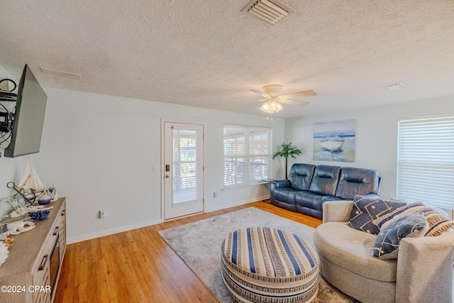 living room with ceiling fan, a textured ceiling, and light wood-type flooring