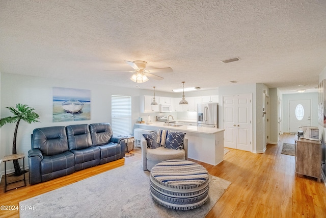 living room with a textured ceiling, light wood-type flooring, plenty of natural light, and ceiling fan