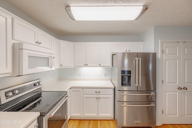 kitchen featuring a textured ceiling, stainless steel appliances, white cabinetry, and light hardwood / wood-style floors