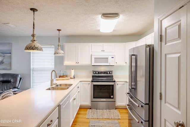 kitchen featuring sink, hanging light fixtures, appliances with stainless steel finishes, light hardwood / wood-style floors, and white cabinetry