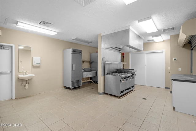 kitchen featuring fridge, stainless steel gas stove, a textured ceiling, and sink