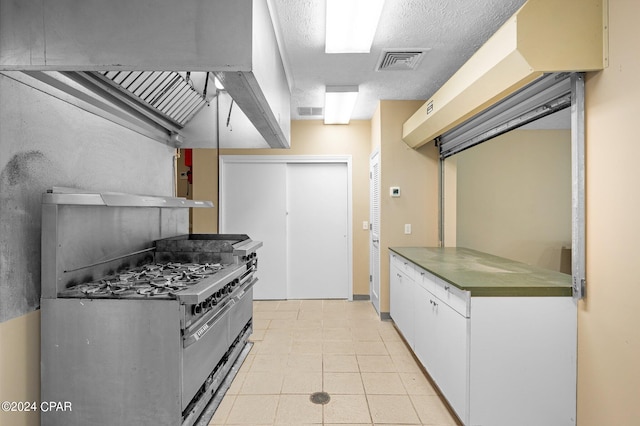 kitchen featuring stainless steel gas range oven, white cabinetry, and light tile patterned flooring