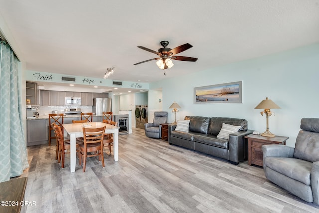 living room with independent washer and dryer, light hardwood / wood-style flooring, and ceiling fan