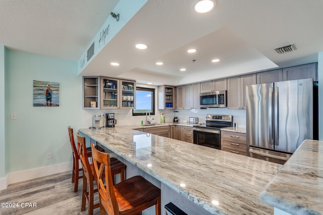 kitchen with light stone counters, kitchen peninsula, stainless steel appliances, light wood-type flooring, and a kitchen bar