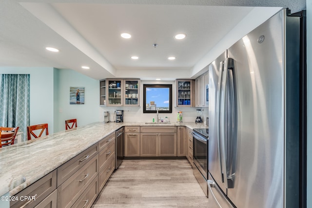 kitchen featuring light stone counters, sink, kitchen peninsula, light hardwood / wood-style flooring, and stainless steel appliances