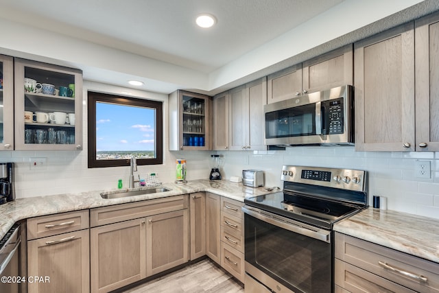 kitchen featuring stainless steel appliances, light hardwood / wood-style floors, sink, and light stone counters