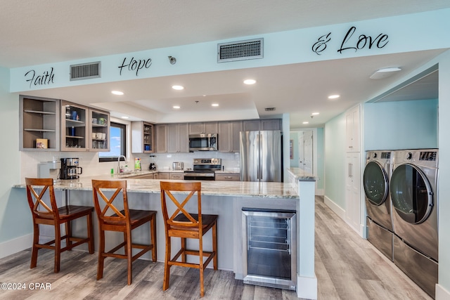 kitchen with beverage cooler, stainless steel appliances, washer and dryer, and kitchen peninsula