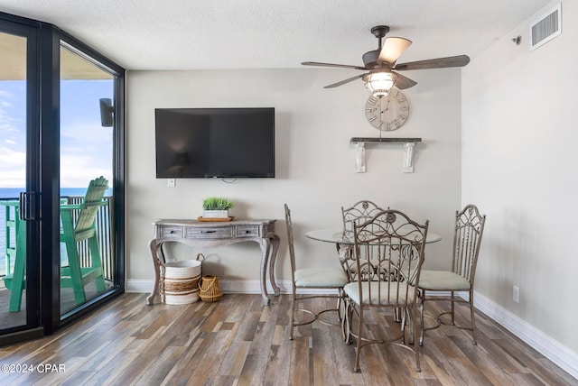 dining space featuring ceiling fan, a textured ceiling, a wall of windows, and hardwood / wood-style floors