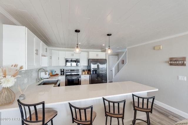 kitchen featuring kitchen peninsula, appliances with stainless steel finishes, decorative light fixtures, white cabinets, and sink