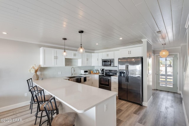 kitchen featuring white cabinets, a kitchen bar, stainless steel appliances, sink, and hanging light fixtures